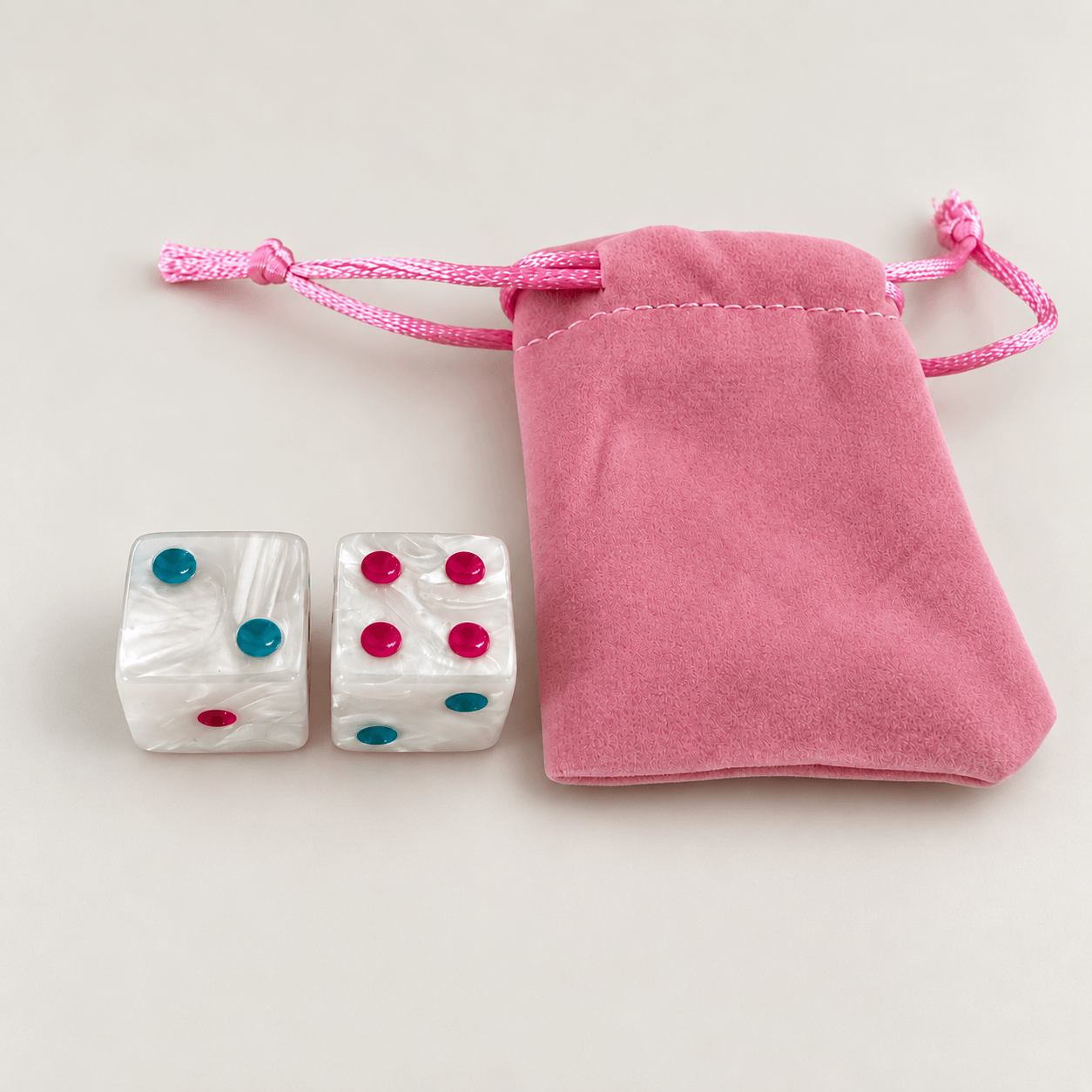 Two pearlescent Mahj-Onn dice beside their pink velvet drawstring pouch