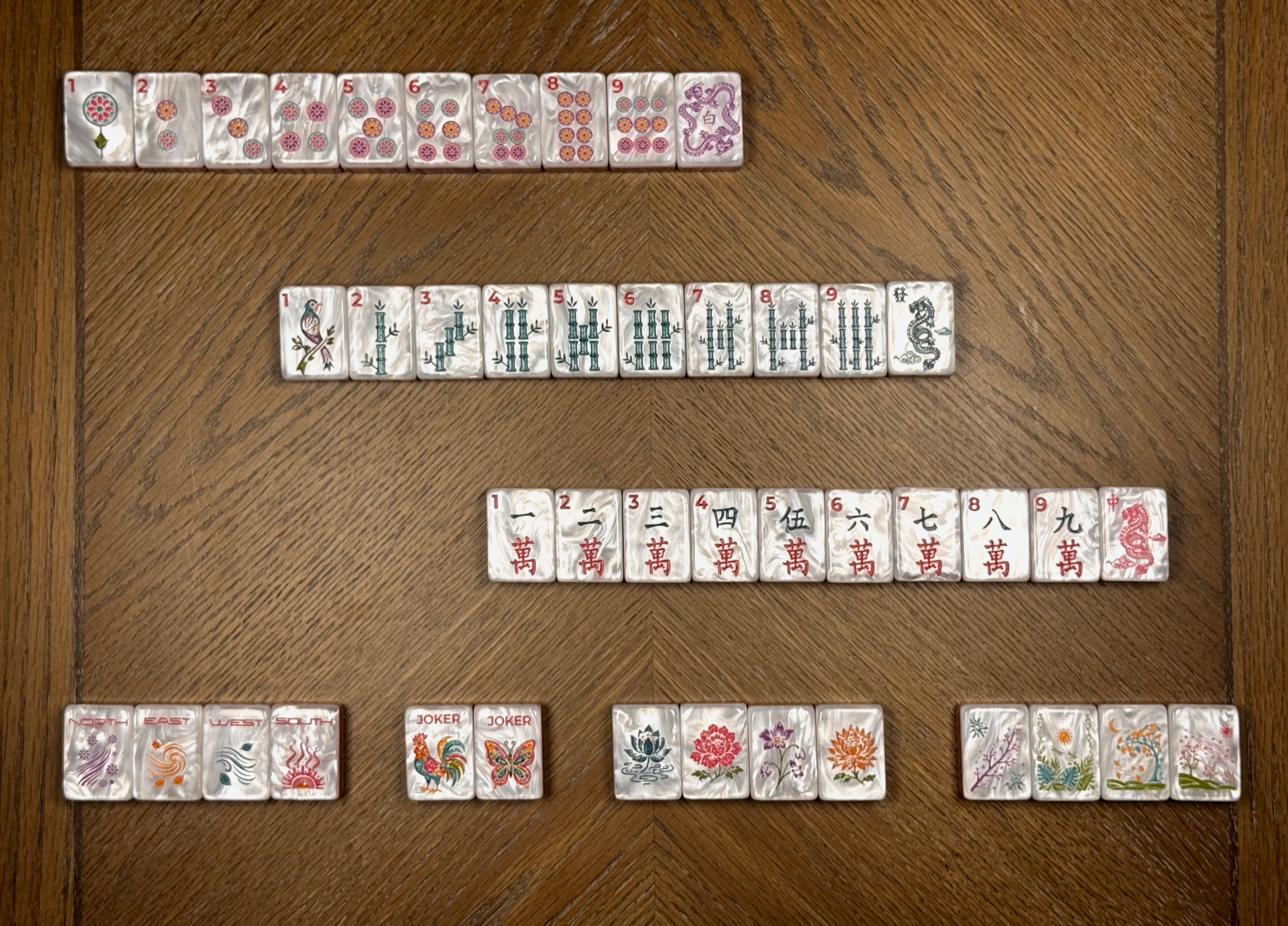 Mahj-Onn Signature dot, bamboo, character, wind, flower, joker, and dragon tiles arranged by suit on a walnut table